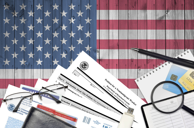 American flag with immigration paperwork on top and a pen and glasses