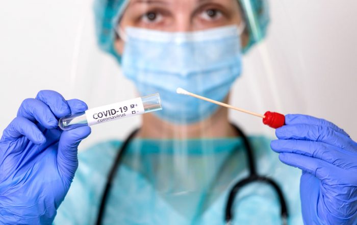 covid test with a swab held by a medical professional wearing a mask