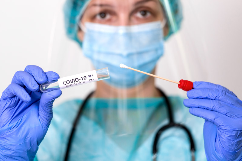 covid test with a swab held by a medical professional wearing a mask